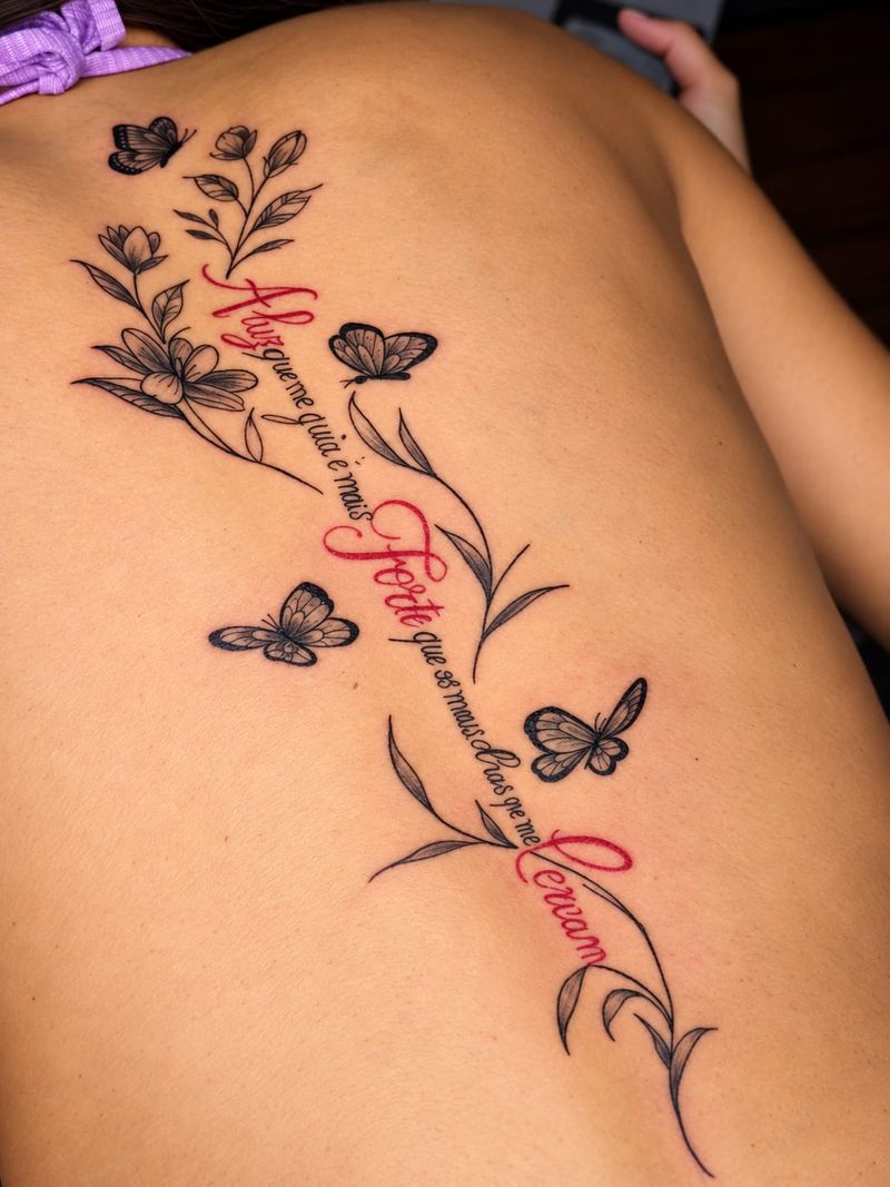 Tatuagem em traço fino de frase em letra cursiva, com flores e borboletas, nas costas