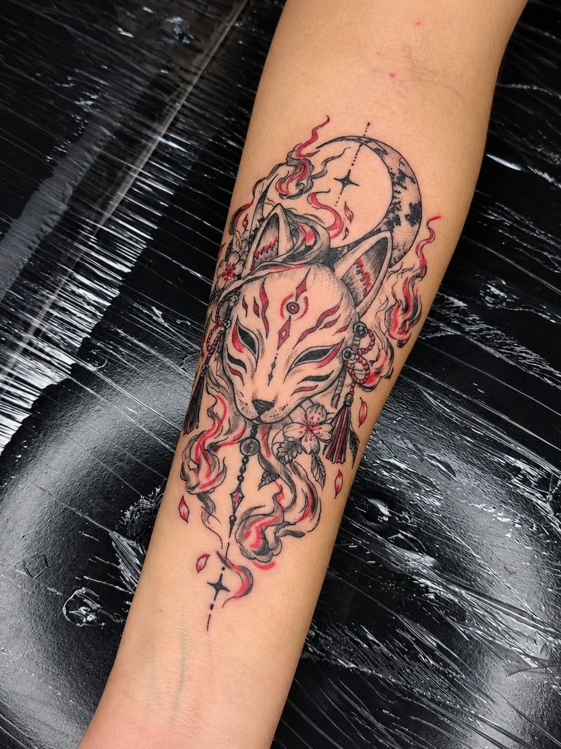 Tatuagem de máscara kitsune com lua crescente, flores de cerejeira e chamas em preto e vermelho no antebraço
